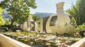 A serene pond with lotus flowers and decorative vases, surrounded by lush greenery and a mountainous backdrop. - Hotel Villa Groff (Ora)