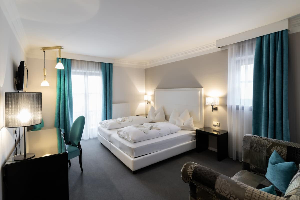 A hotel room with a large bed, a desk with a lamp, a chair, and a sofa.