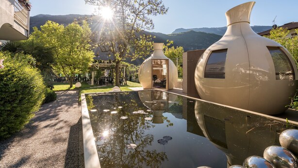 A modern building with a unique architectural design, featuring large vases and a reflective pool. - Hotel Villa Groff (Ora)