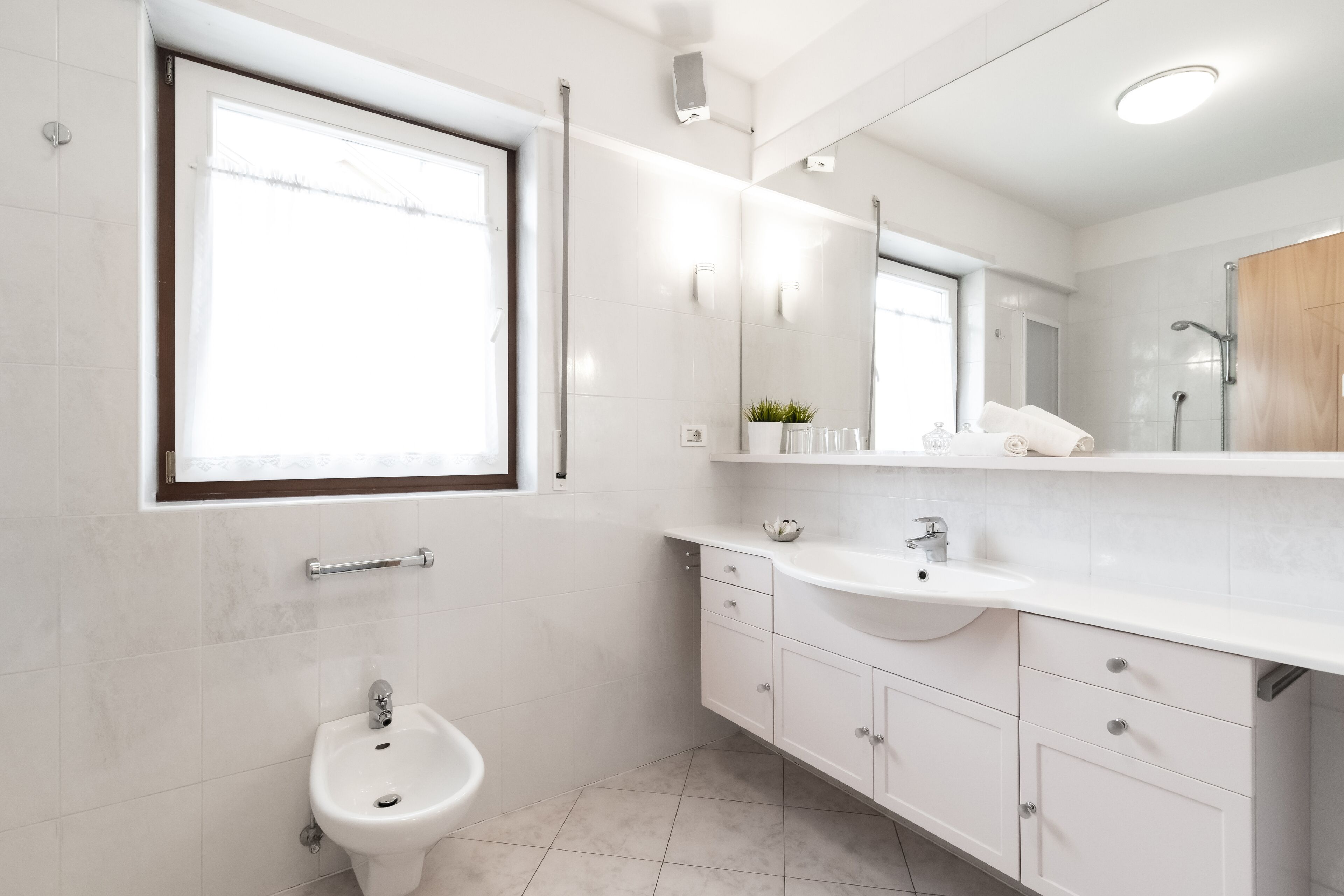 Un baño moderno con un bidé, un lavamanos, un espejo y una ventana.