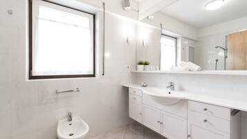 Un baño moderno con un bidé, un lavamanos, un espejo y una ventana.