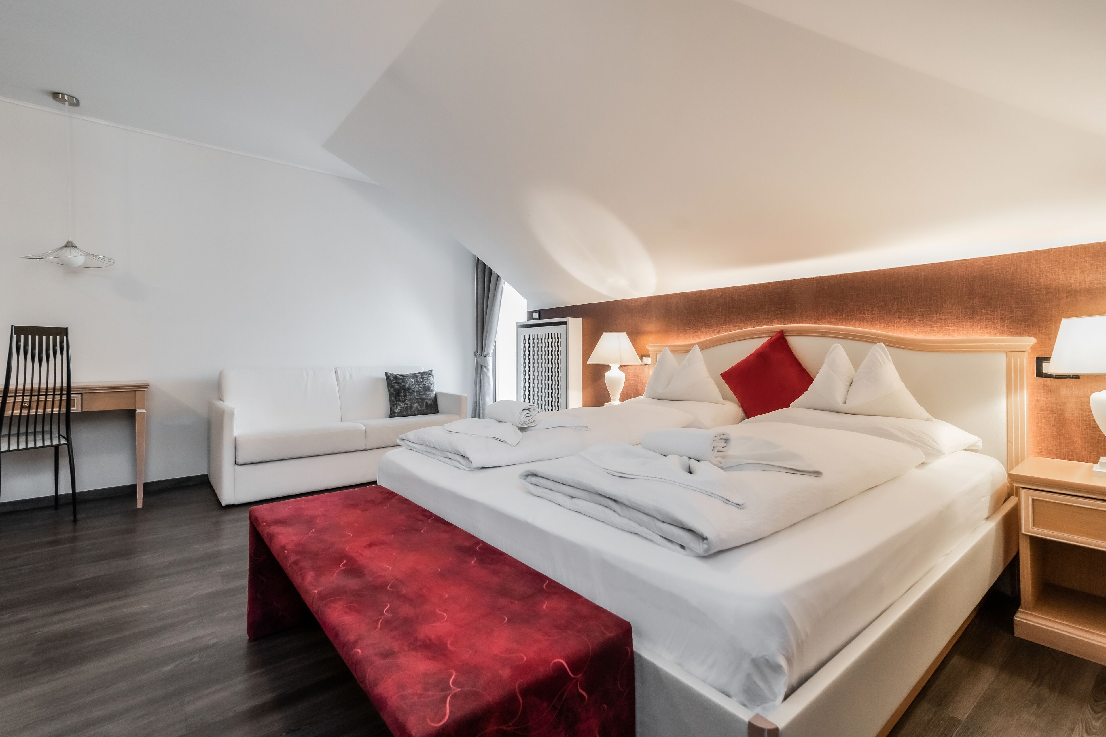Ein modernes Hotelzimmer mit einem großen Bett, einer roten Bank, einem Schreibtisch und einem Stuhl.