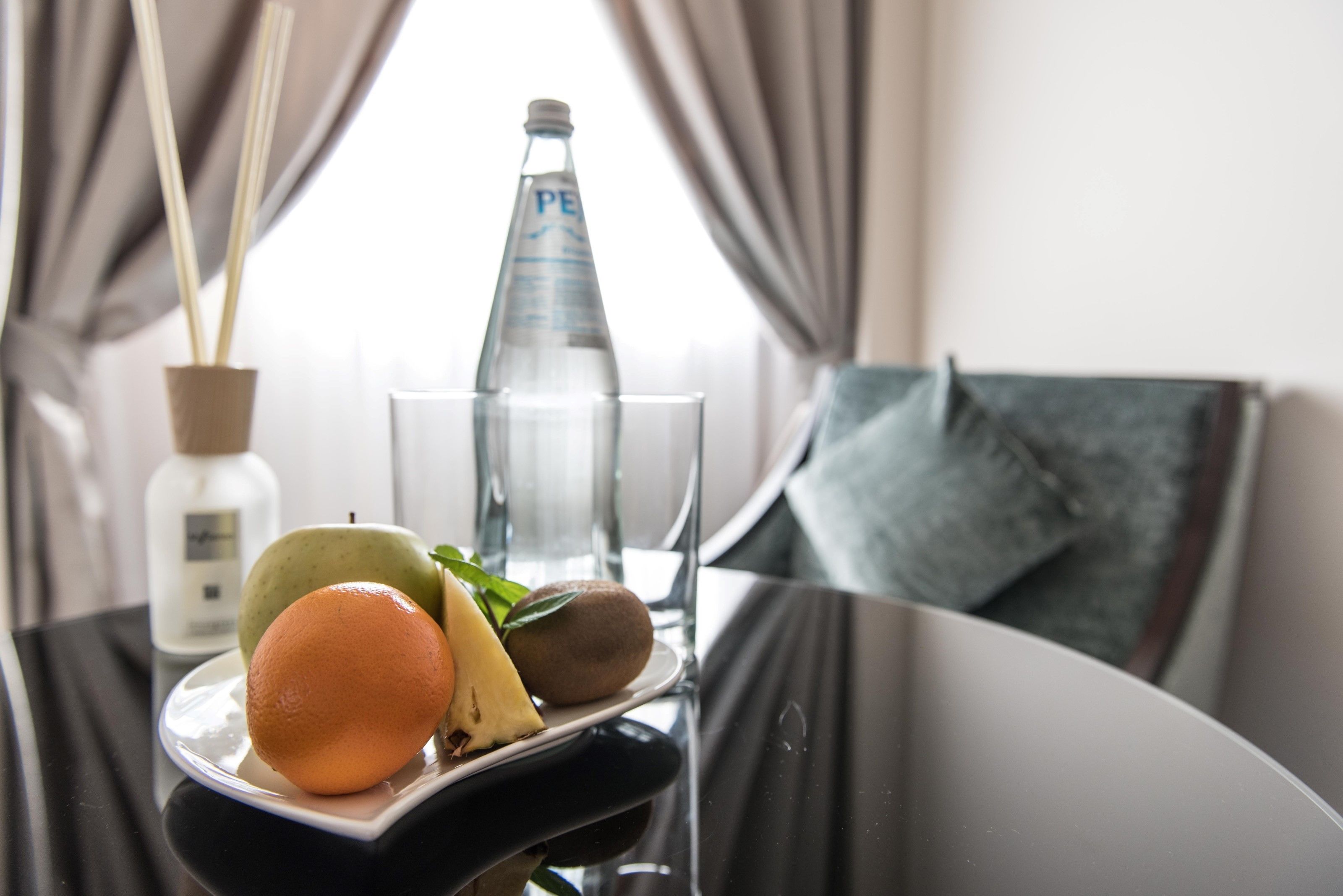 Une table avec une assiette de fruits, un verre et une bouteille d’eau dans une chambre d’hôtel.