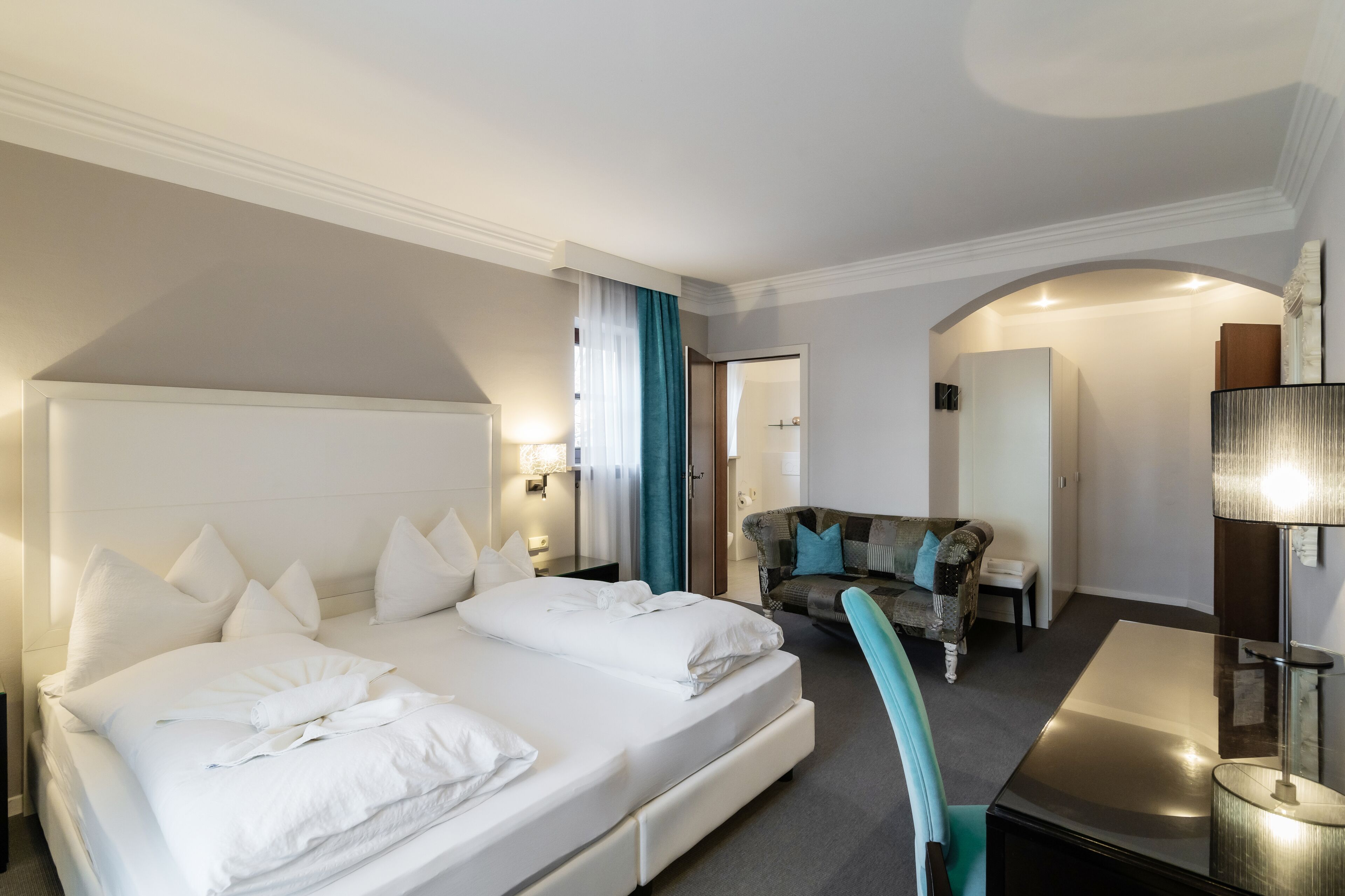 A hotel room with a large bed, a sofa, a desk, and a lamp.