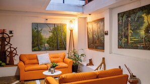 A living room with an orange sofa, a small round table, and two paintings on the wall. - Hotel La Casona (Iquitos)