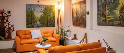 A living room with an orange sofa, a small round table, and two paintings on the wall.