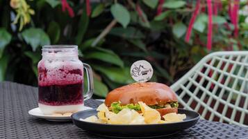 Una comida con hamburguesa y papas fritas, una bebida en frasco y un plato de bocadillos sobre una mesa al aire libre.