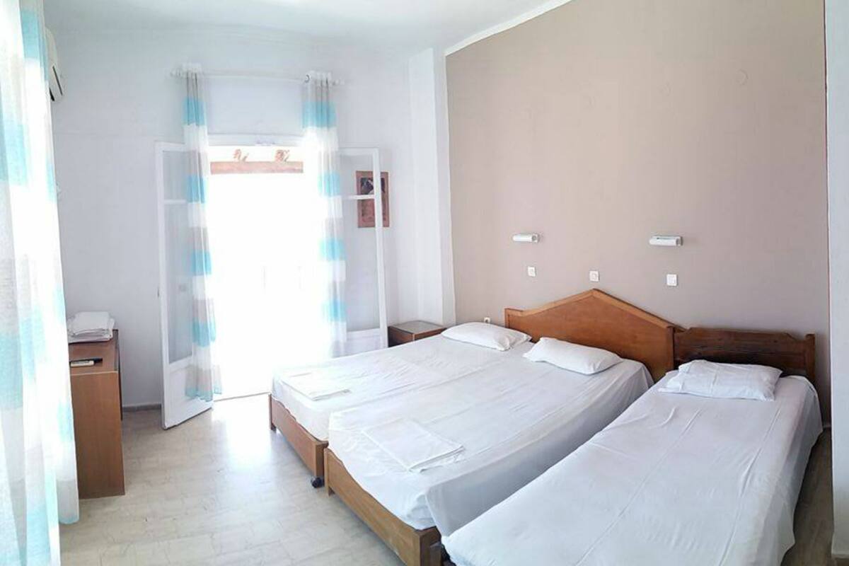 A hotel room with two beds, a wooden headboard, a small kitchenette, and a bathroom with a shower curtain.