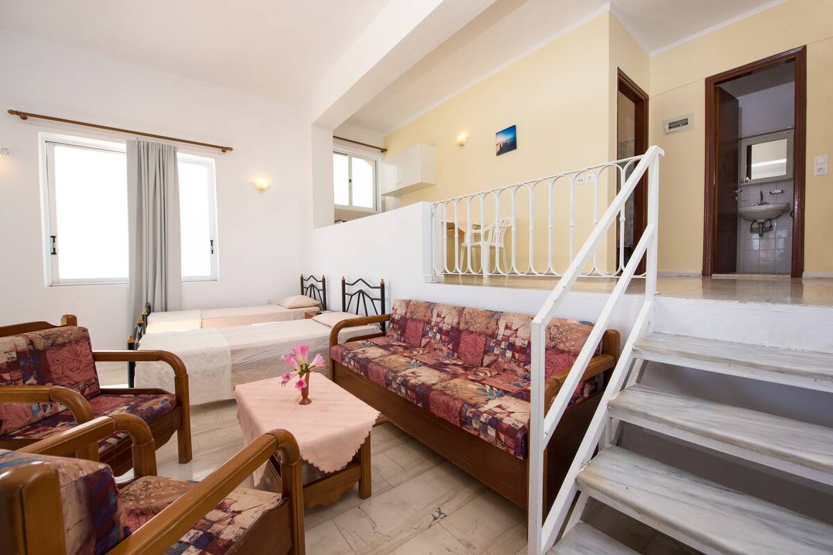 A spacious living area with a sofa, chairs, a small table, and a staircase leading to an upper floor.