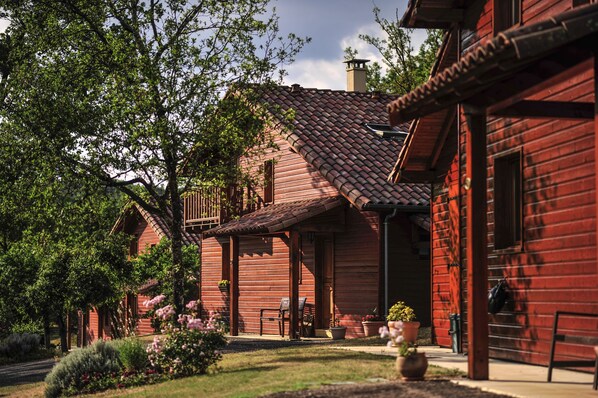 A traditional wooden building with a red-tiled roof, a porch with seating, and a garden with various plants.