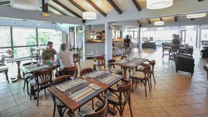 A spacious restaurant with multiple dining tables and chairs, a bar area, and large windows offering views of the outdoors.