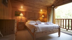 A wooden cabin bedroom with a bed, two bedside lamps, a dresser, and a view of the outdoors.