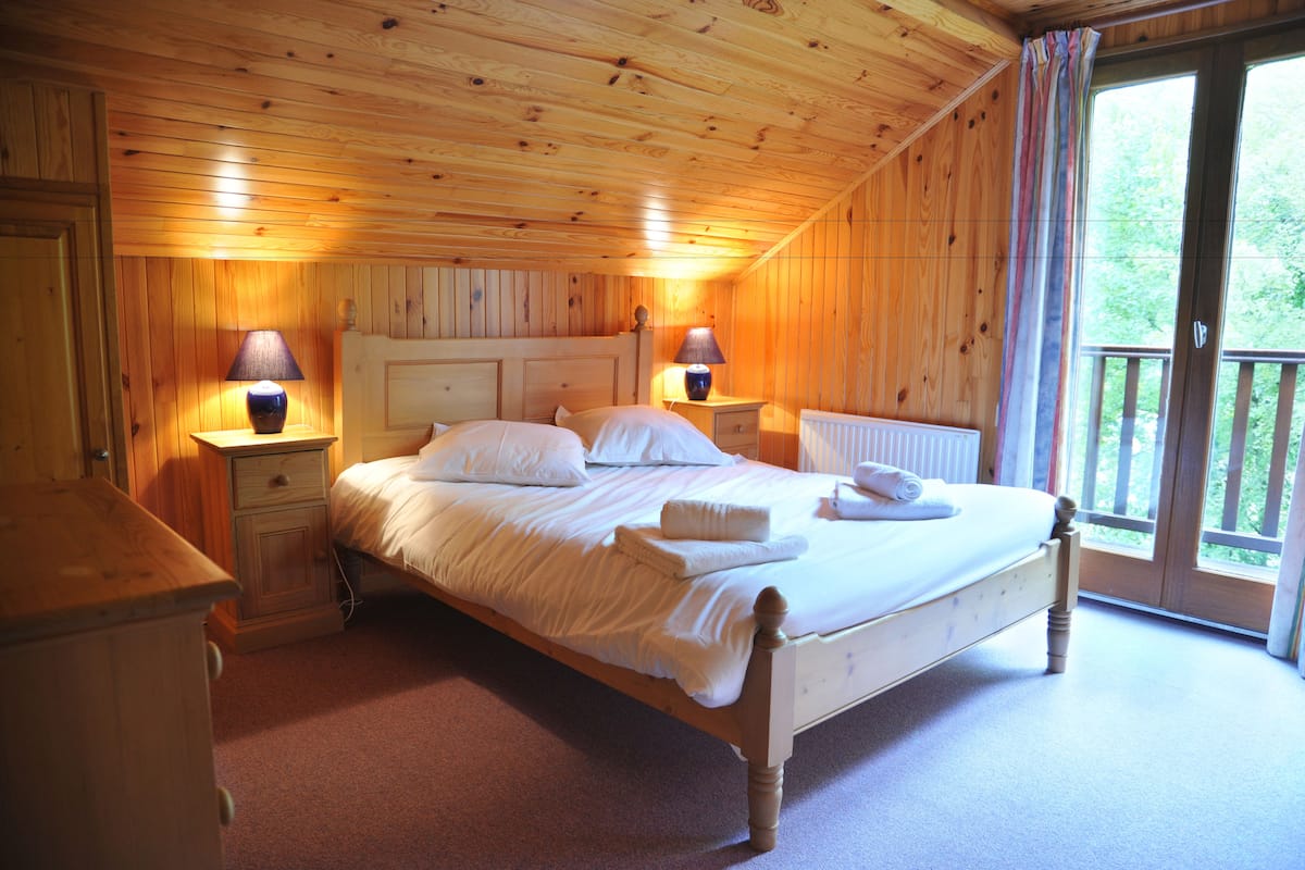 Un dormitorio con paneles de madera, una cama, dos lámparas de noche y vistas amplias a través de un ventanal.
