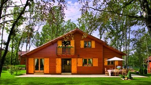 A wooden cabin with a balcony, large windows, and a patio area.