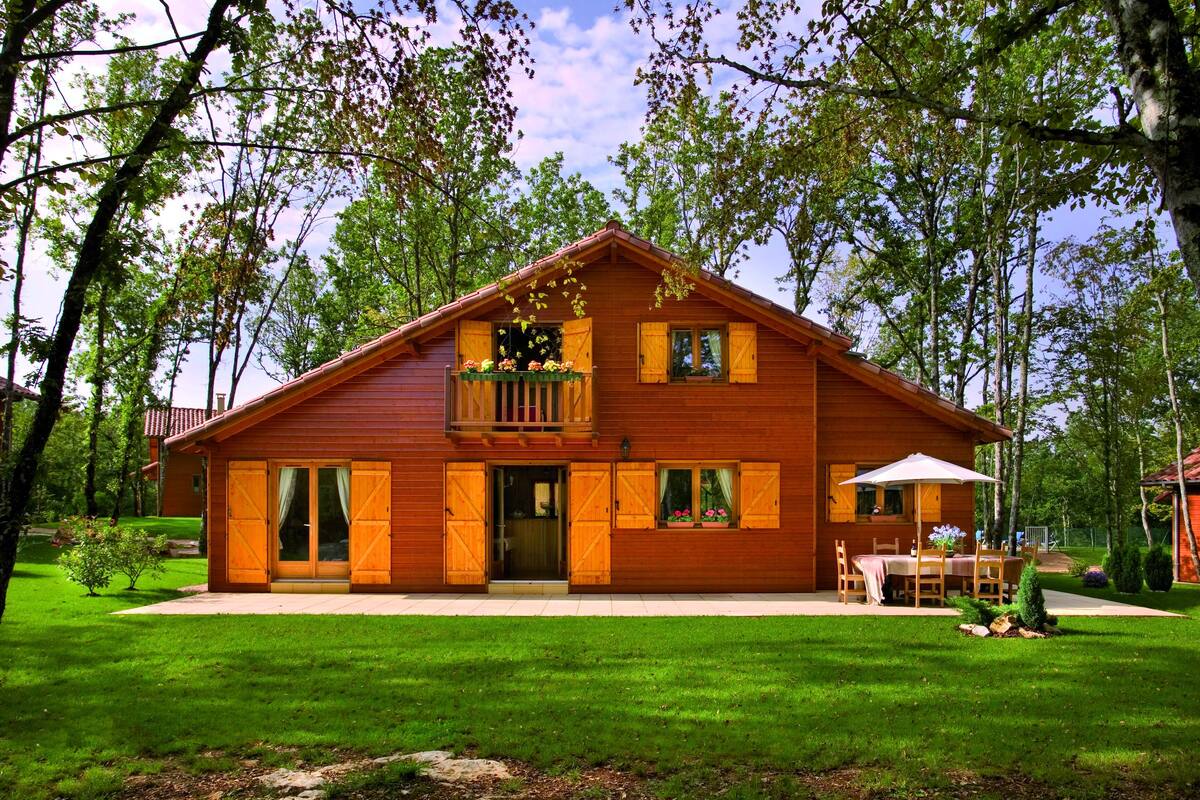 Una cabaña de madera con balcón, ventanas grandes y un patio.