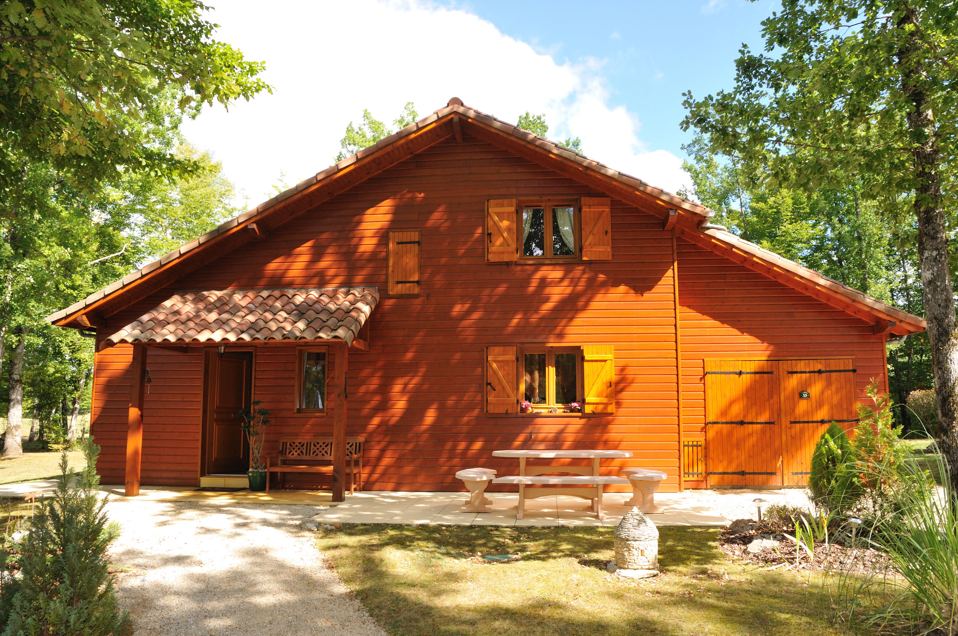 A wooden cabin with a tiled roof, a porch with a bench, and a picnic table.