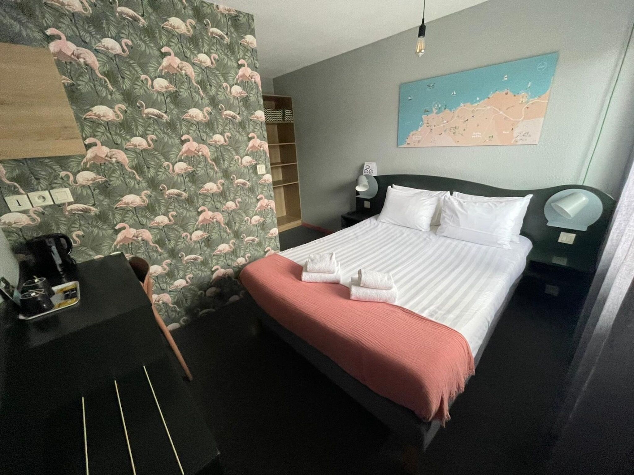 A hotel room with a bed, a desk, a map on the wall, and a nightstand.