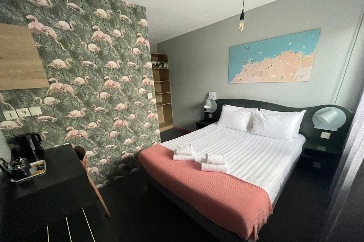 A hotel room with a bed, a desk, a map on the wall, and a nightstand.