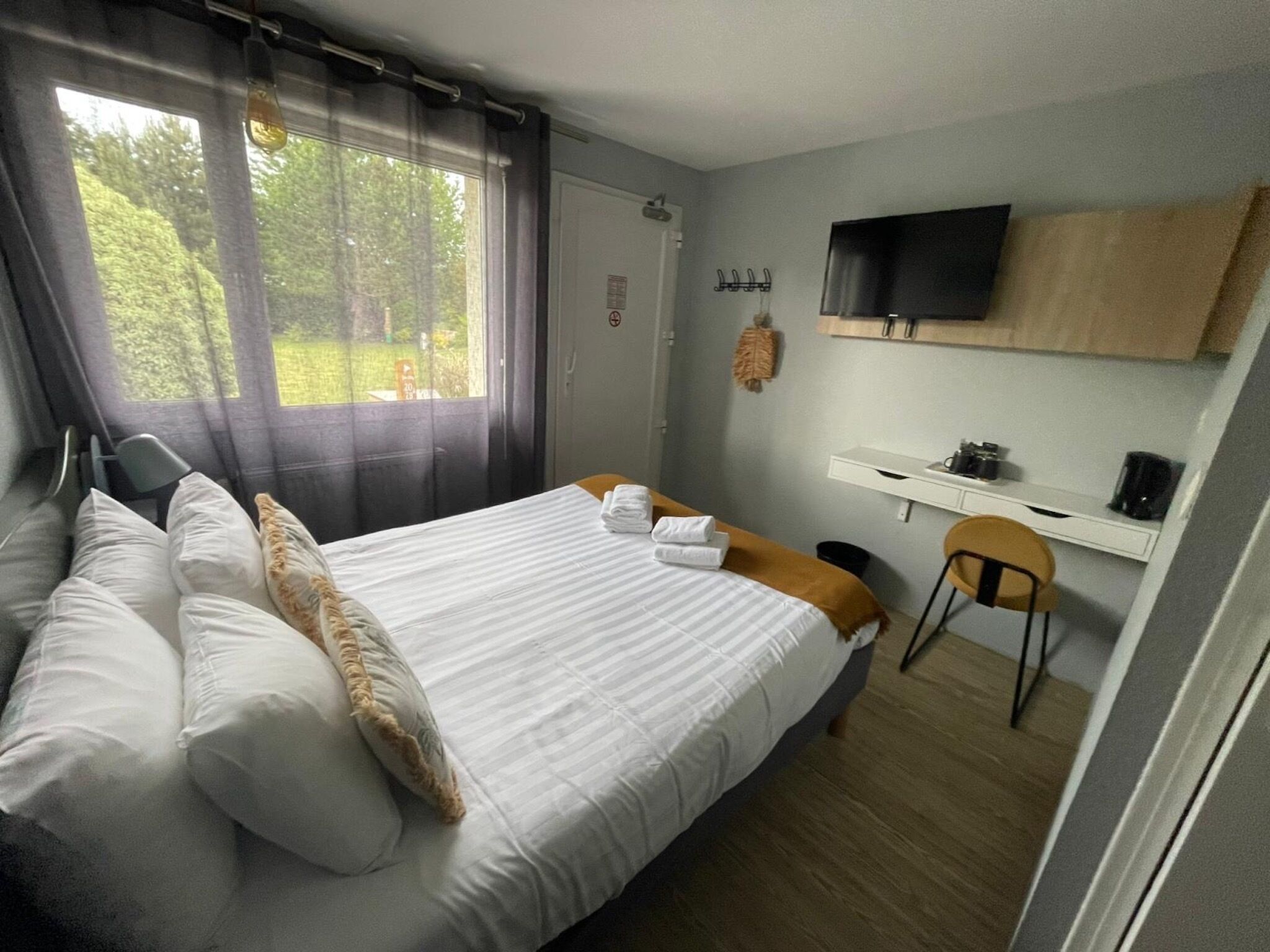 A bedroom with a bed, a chair, a desk, a TV, and a window with curtains.