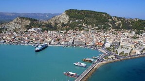 Vista aèria d'una població costanera amb un port esportiu, edificis i turons al fons.