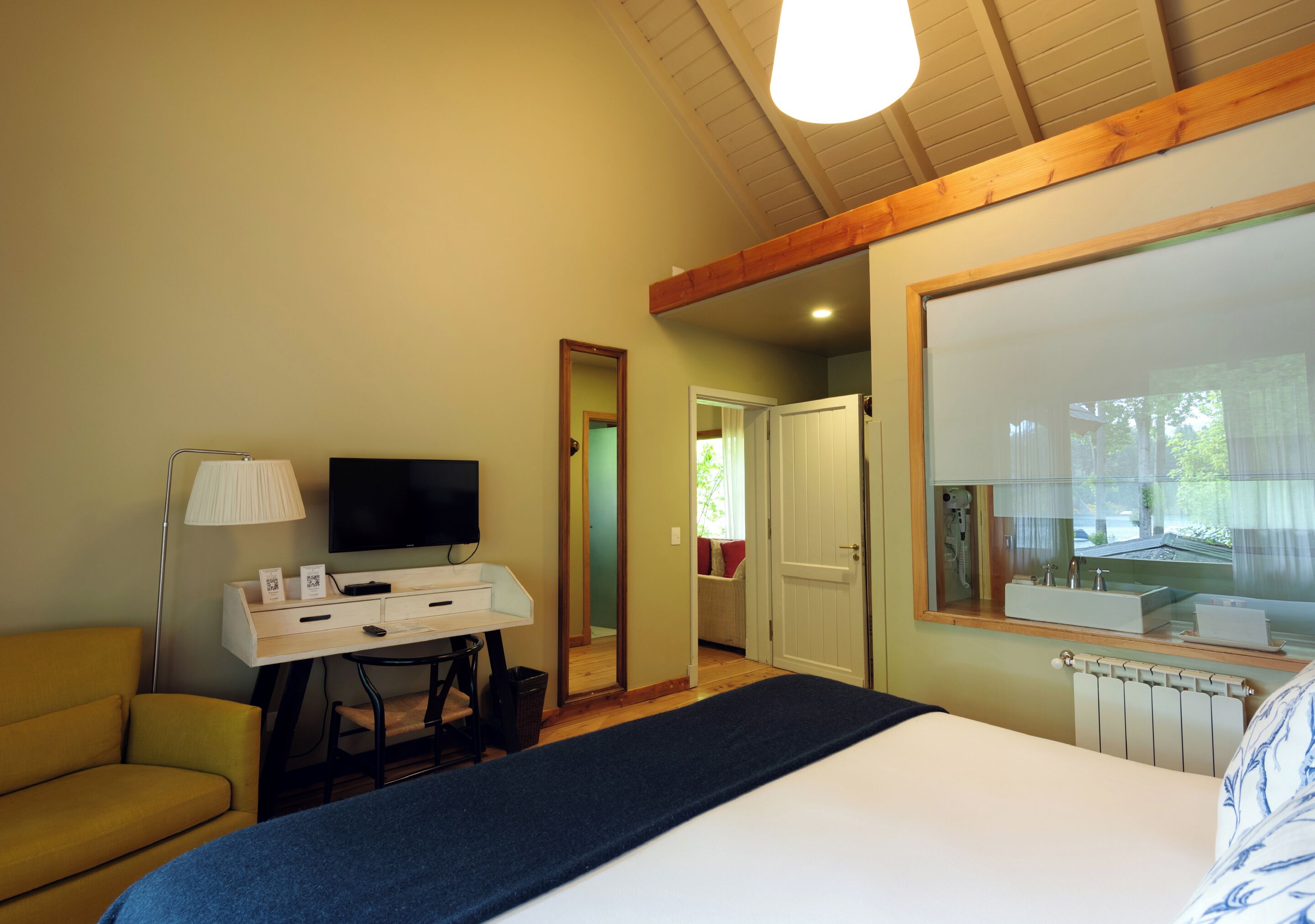 Une chambre à coucher avec un lit, un bureau avec une télévision, une lampe et une vue sur l’extérieur.