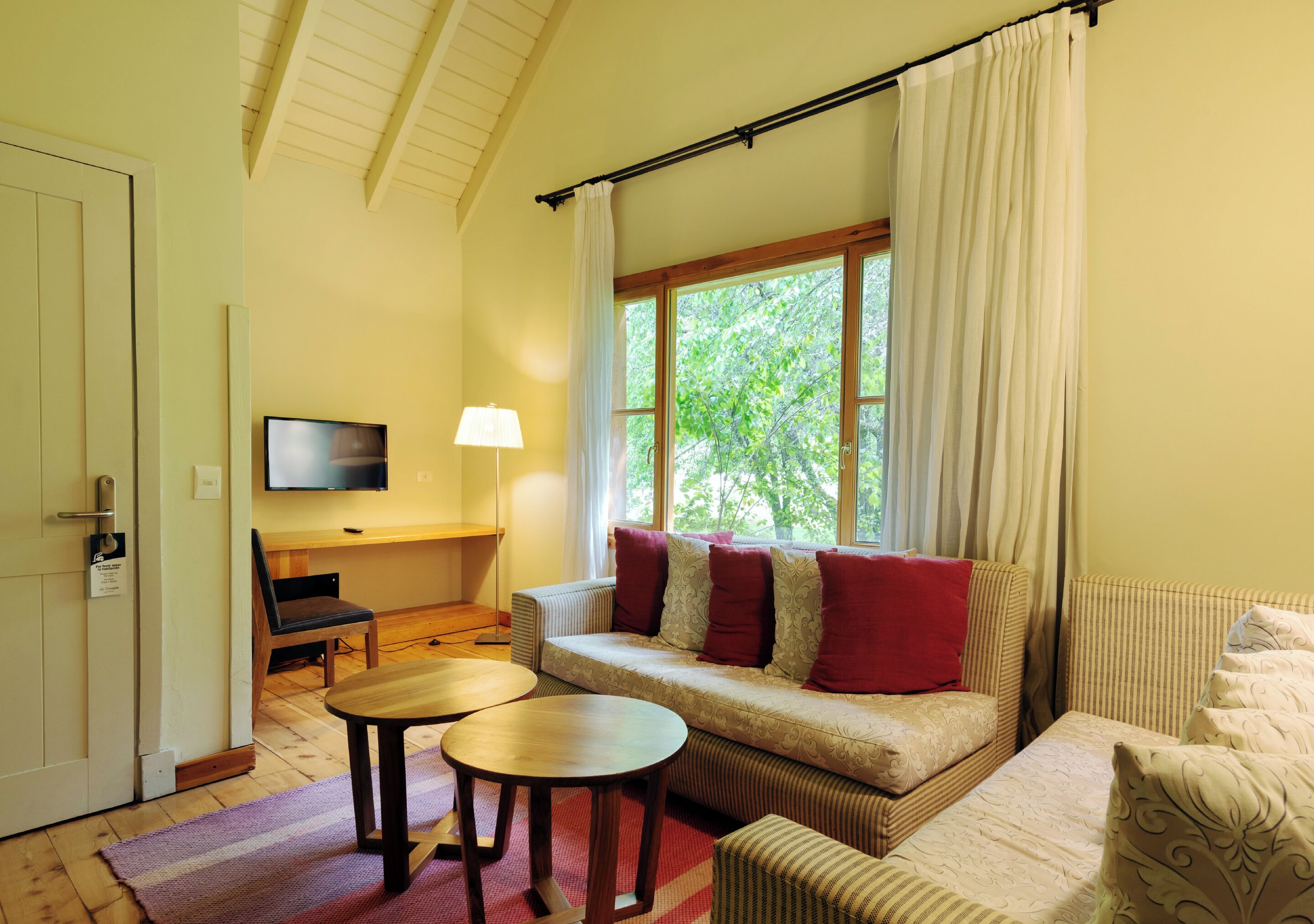Una sala de estar acogedora con sofá, televisión, una mesita y una ventana con cortinas.