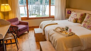 A cozy bedroom with a bed, a desk, a chair, and a window with a view of trees and a lake.