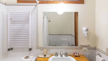 Un bagno con un lavandino bianco, due rubinetti, uno specchio, un portasciuga-asciugamani, una tenda da doccia e un asciugacapelli.