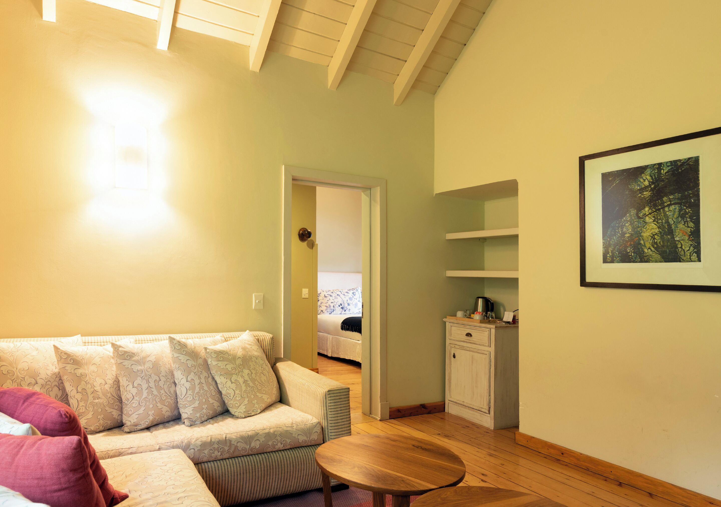 A cozy living room with a sofa, a small wooden table, and a kitchen area with cabinets and a framed picture on the wall.