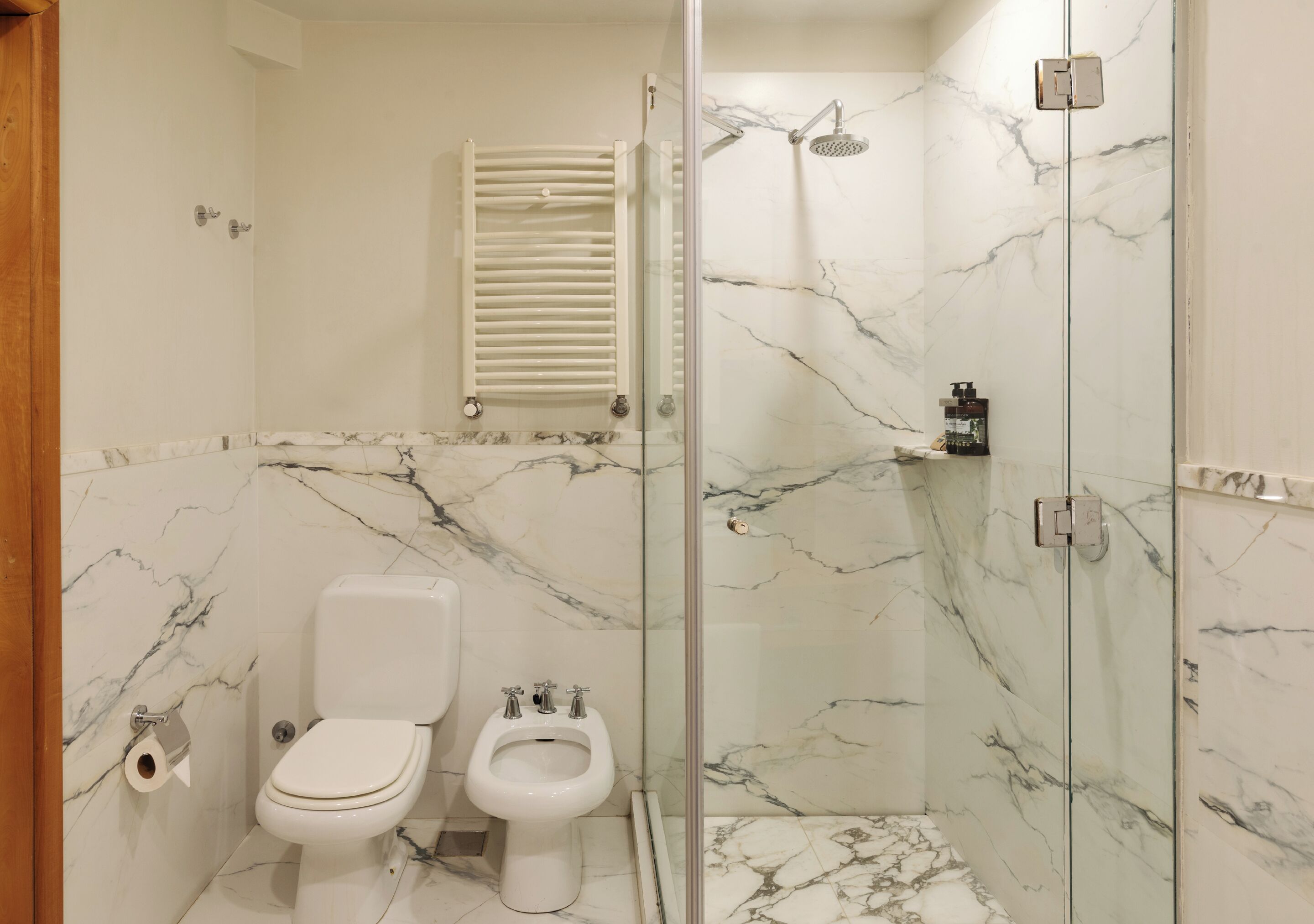 Un baño con inodoro, bidé y ducha con mampara de vidrio y paredes de mármol.
