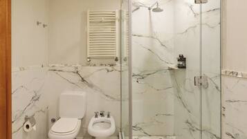 Un baño con inodoro, bidé y ducha con mampara de vidrio y paredes de mármol.