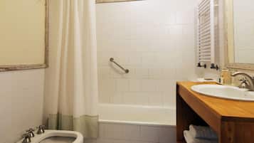 A bathroom with a bathtub, a bidet, a sink, and a wooden vanity.