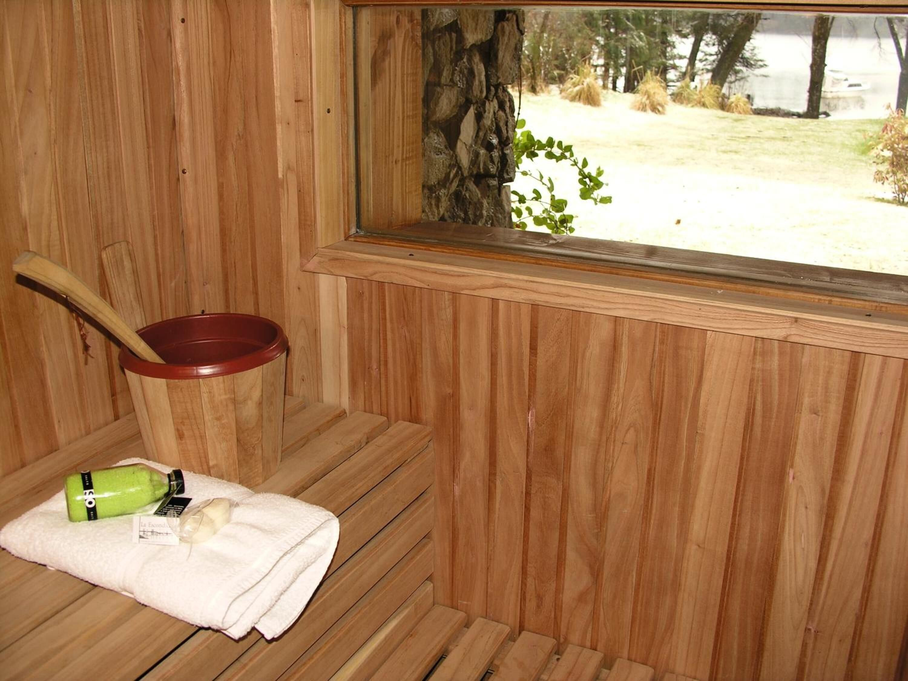 Una sauna de madera con ventana, un recipiente rojo, una toalla y una botella de loción.