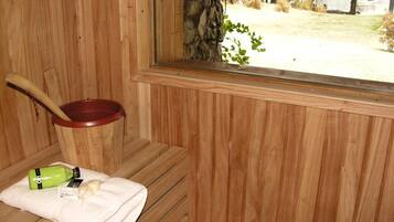 Una sauna de madera con ventana, un recipiente rojo, una toalla y una botella de loción.
