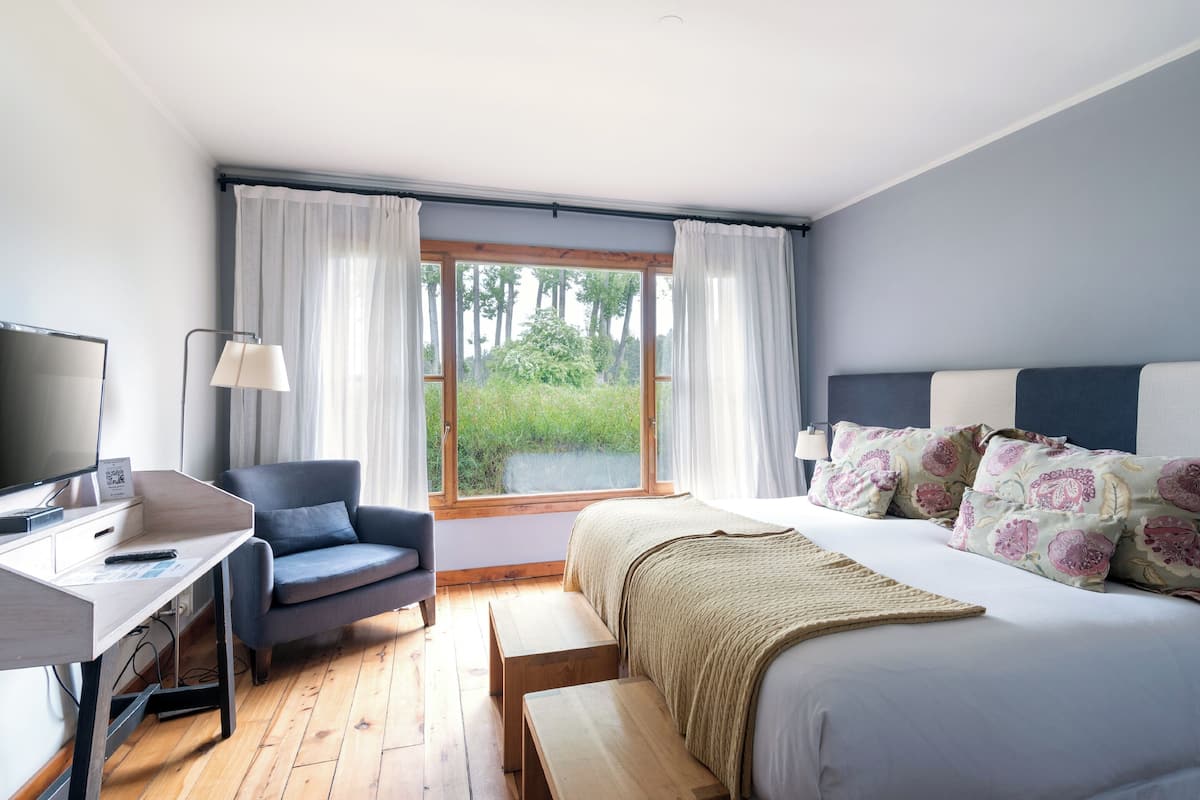 Une chambre à coucher avec un lit, un bureau, une chaise, une télévision et une fenêtre avec des rideaux.