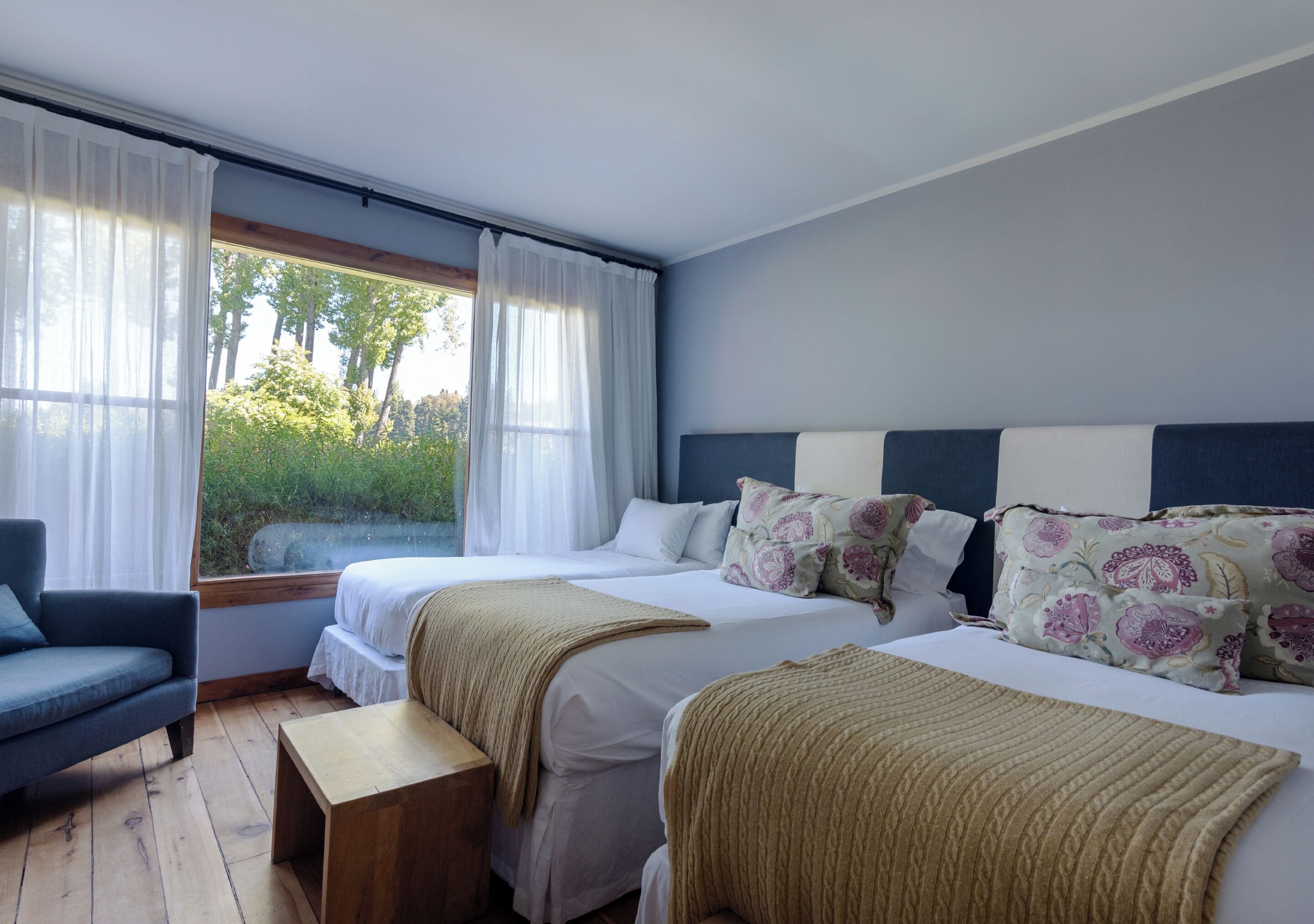 A bedroom with two beds, a chair, and a wooden bench.