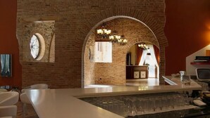 Uma área de bar com parede de tijolos, porta em arco e um candelabro.