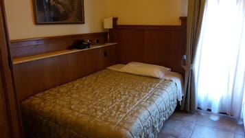 Una habitación de hotel con cama, teléfono, un cuadro en la pared y ventana con cortinas.