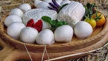 A wooden tray filled with white cheese balls, a large cheese wheel, and some vegetables.