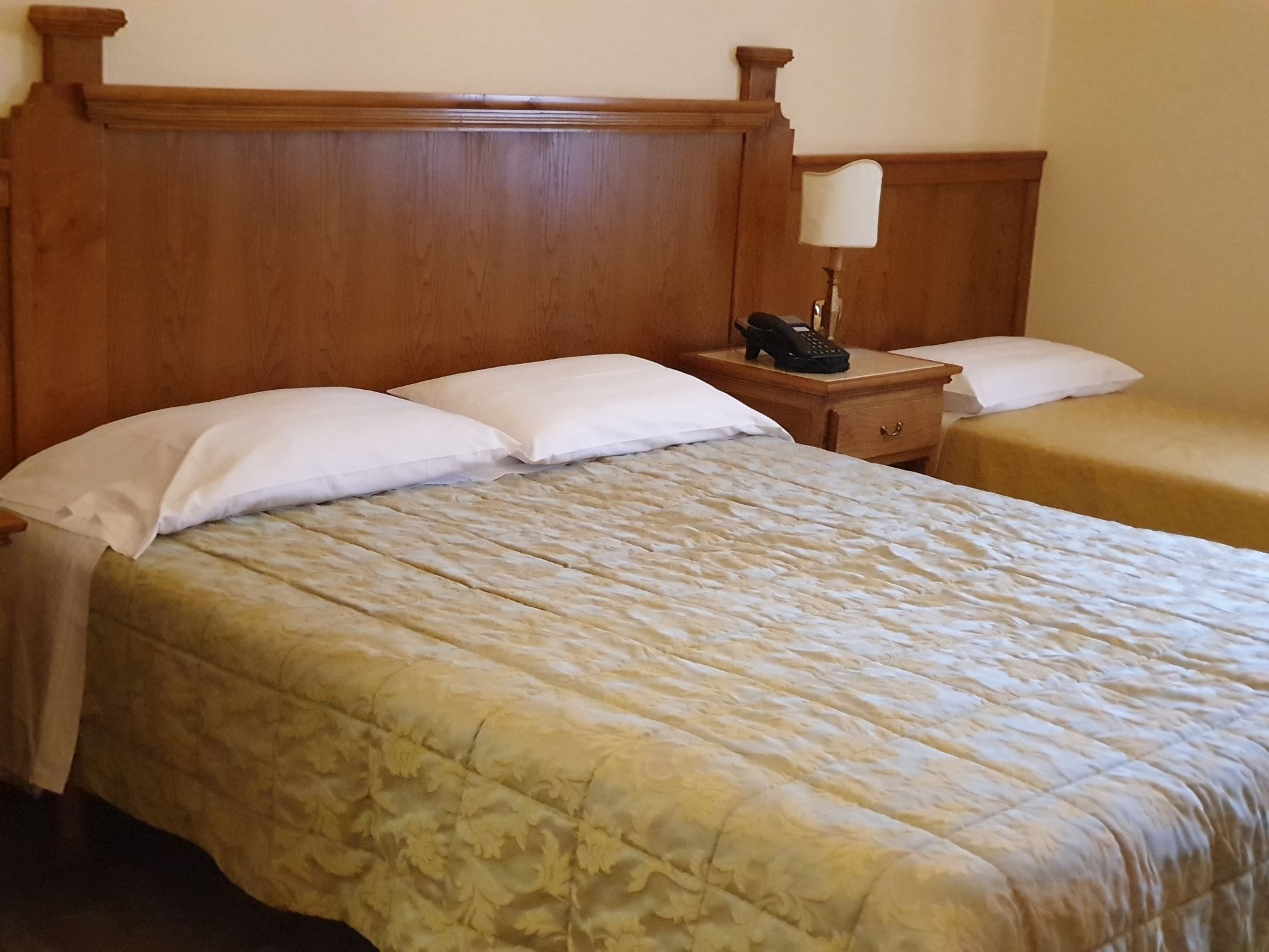 A hotel room with a large bed, two bedside tables, a nightstand, a lamp, and a telephone.