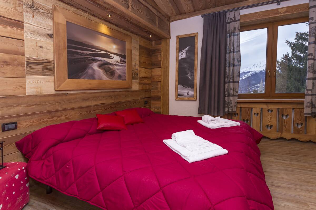 A wooden cabin bedroom with a large bed, red bedding, and two framed pictures on the wall.