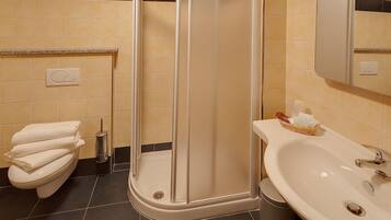 Un baño con inodoro, ducha con puerta de vidrio y lavamanos con espejo.