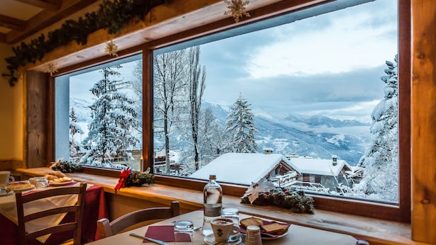 A cozy dining area with a table set for two, a window with a snowy mountain view, and a wooden ceiling. - Hotel Sauze (Sauze d'Oulx)