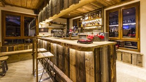 A rustic bar area with wooden bar counter, stools, and shelves of bottles. - Hotel Sauze (Sauze d'Oulx)