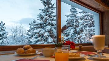 Una mesa con un plato de pasteles, un vaso de líquido ámbar y un vaso de líquido blanco, frente a un paisaje nevado visible a través de una ventana.
