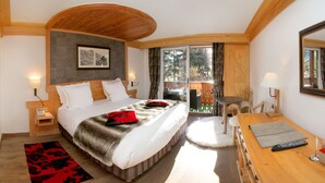 Un dormitorio con una cama grande, techo de madera, una mesita con lámpara y vistas al exterior.