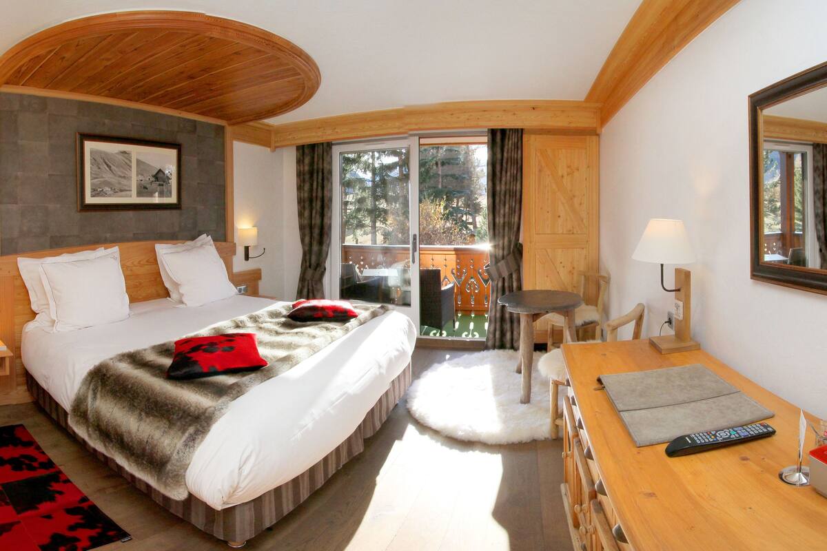 Un dormitorio con una cama grande, techo de madera, una mesita con lámpara y vistas al exterior.