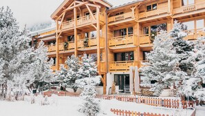 Un edificio de madera de varios pisos con balcones, rodeado de árboles cubiertos de nieve.