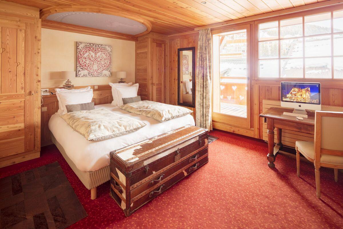 Una habitación de madera con una cama, un escritorio con computadora y una ventana que da a un paisaje nevado.