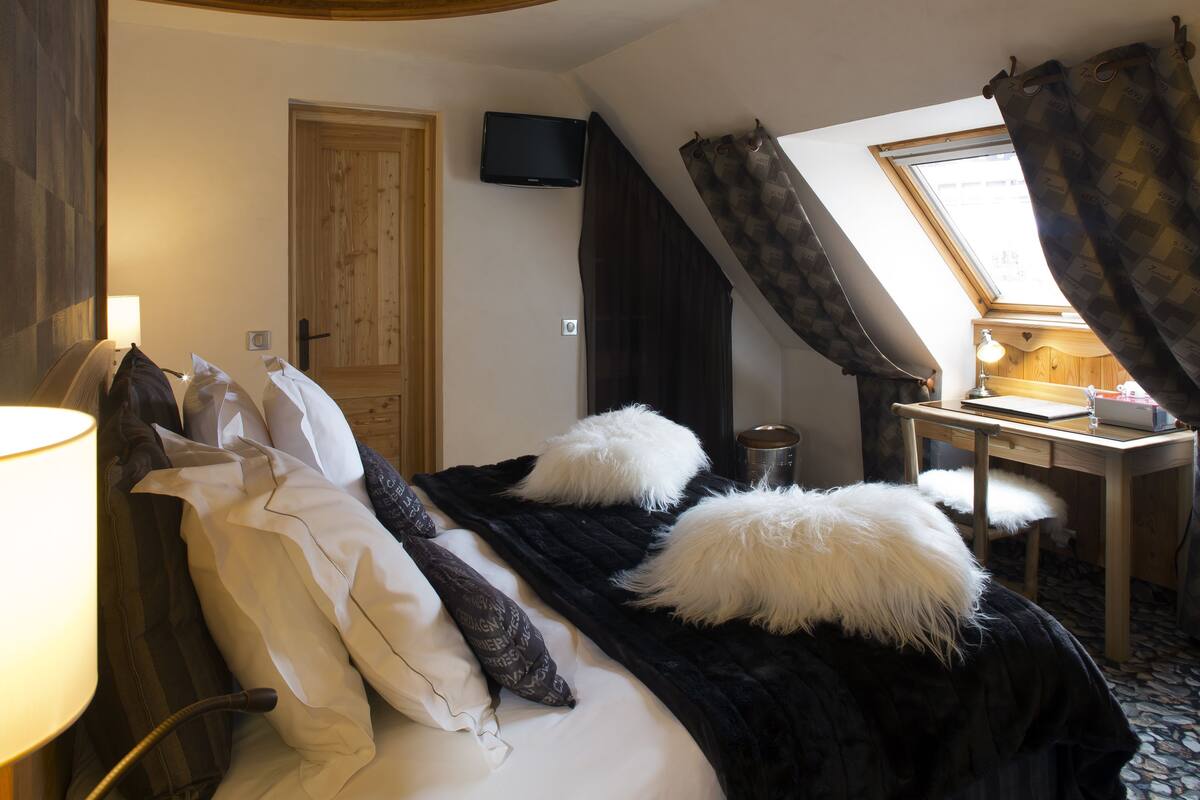 Un dormitorio con cama, escritorio, silla, televisor y ventana con cortinas.